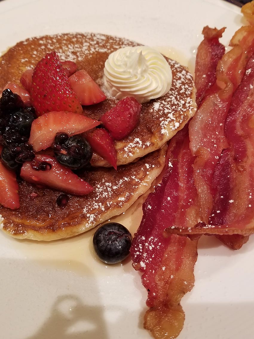 Short Stack Buttermilk Pankcakes with Virginia Maple syrup, honey butter, powdered sugar, macerated seasonal berries, mint, and thick-cut slab bacon