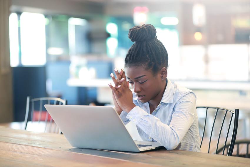 black women with her head down and eyes closed in front of her laptop in an office breakroom