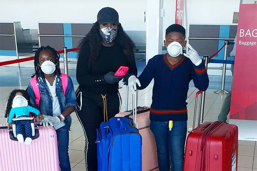 Spice and her children pictured in the Airport with masks, luggage, and gloves.