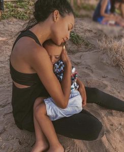 Naya Rivera cradling her son in her arms while sitting in the sand on the beach