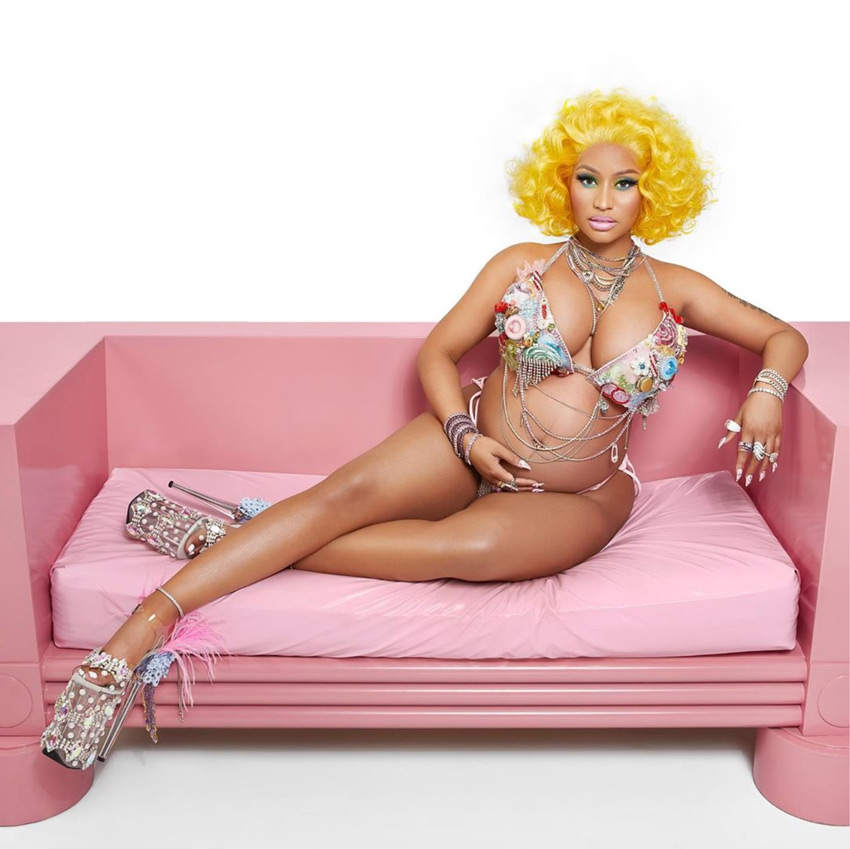 Nicki Minaj in a gold wig and bikini sitting and cradling her pregnant belly.