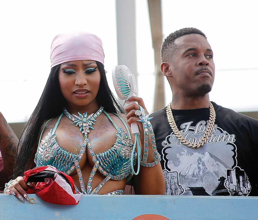 nicki minaj standing next to her husband Kenneth Petty in Trinidad. She clutches a trinidad flag in one hand and a portable fan in her other hand.