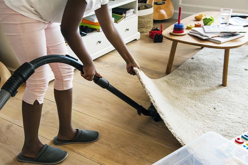 black child lifting a rug to vacuum